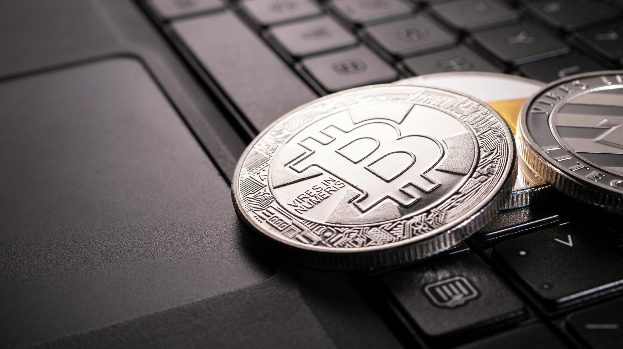 A close-up photograph of silver and gold Bitcoin coins placed on a black keyboard, symbolizing the intersection of digital finance, tech startups, and cryptocurrency growth.